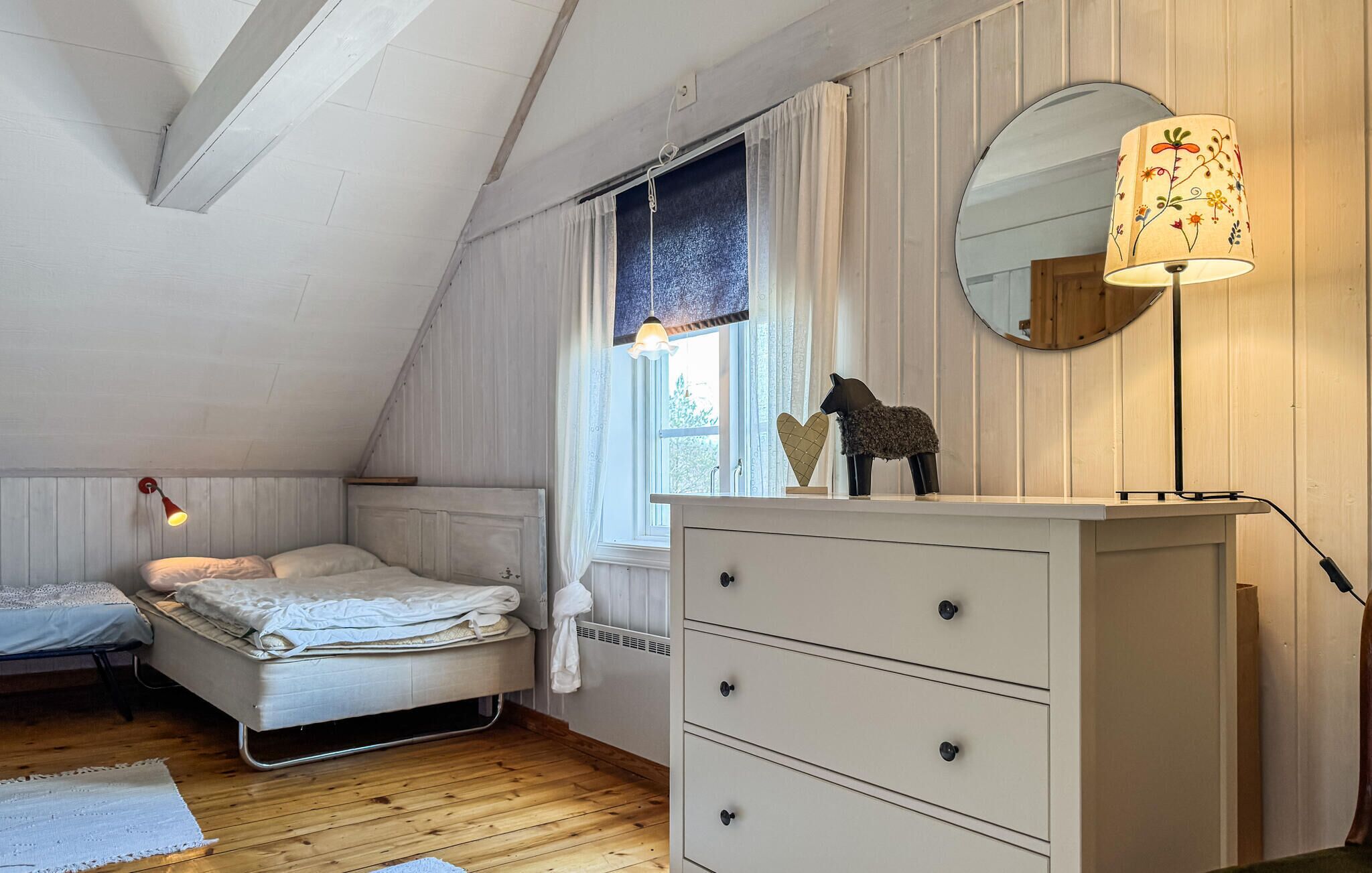 Ein Schlafzimmer mit Bett, Kommode, Spiegel und einem Fenster mit Vorhängen.