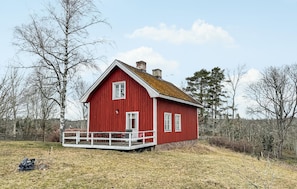 Ein rotes Holzhaus mit Veranda, umgeben von Bäumen und einer grünen Wiese.