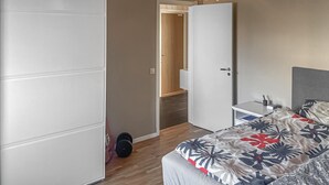 Ett sovrum med en säng, ett skrivbord, en stol, en gitarr och en dörr som leder ut till en hall.