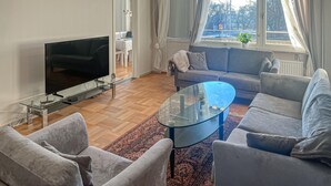 Ett vardagsrum med en platt-TV, två grå soffor, ett soffbord i glas och en mönstrad matta.