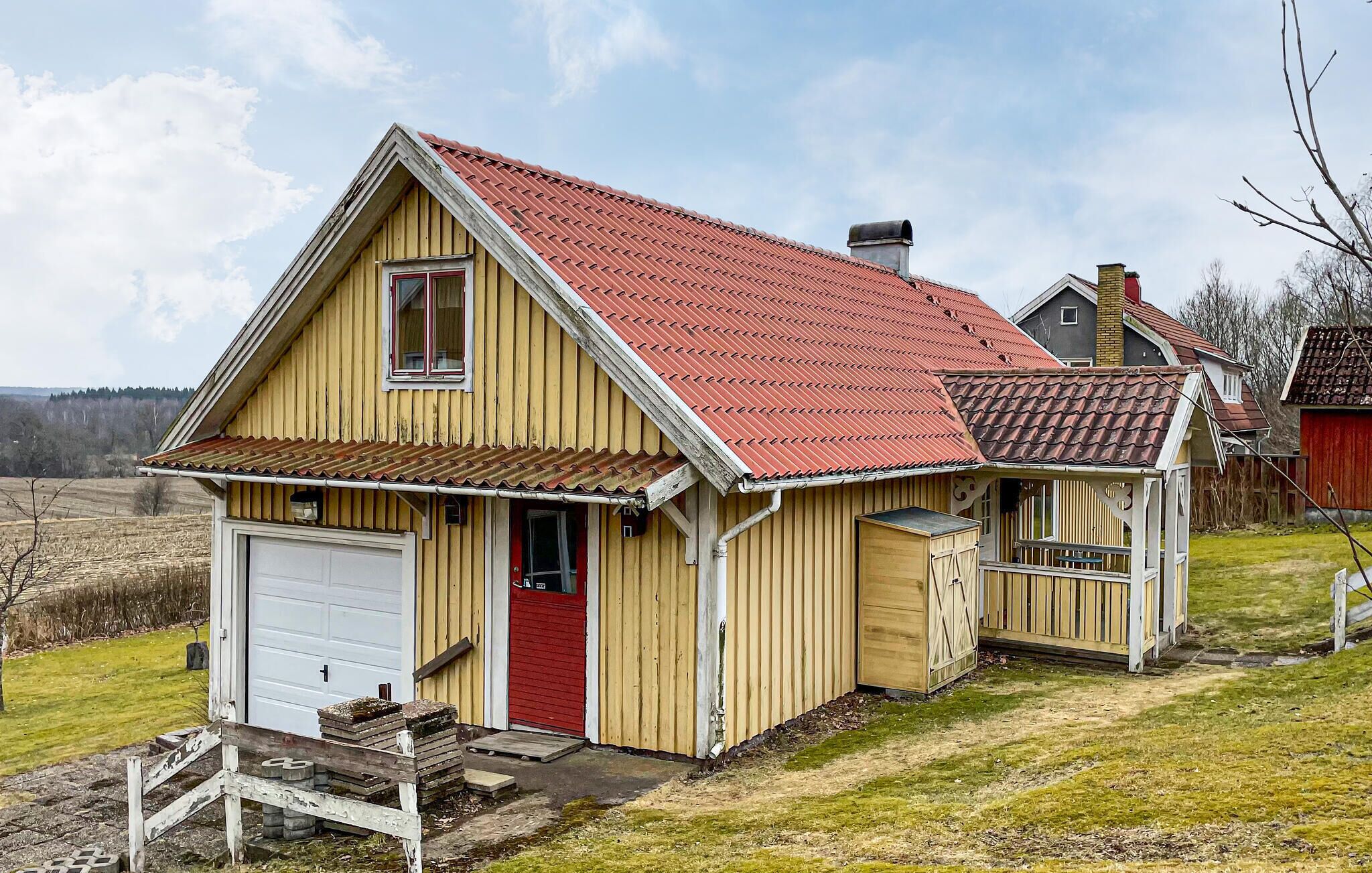 Une maison en bois d’un seul étage, avec un toit rouge, un garage et un petit porche.