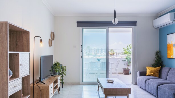 A modern living room with a TV, sofa, and dining table. - Sweet Retreat 2-BR Apt. in Mackenzie (Larnaca)