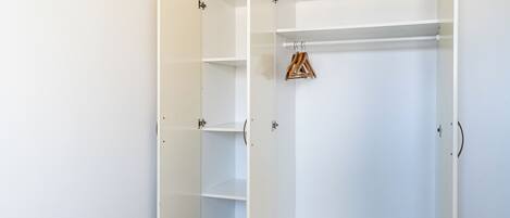Une armoire blanche dotée de nombreuses étagères et d’un espace pour suspendre les vêtements.