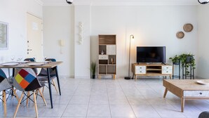 A modern living room with a dining area, a TV, and a wooden coffee table. - Sweet Retreat 2-BR Apt. in Mackenzie (Larnaca)