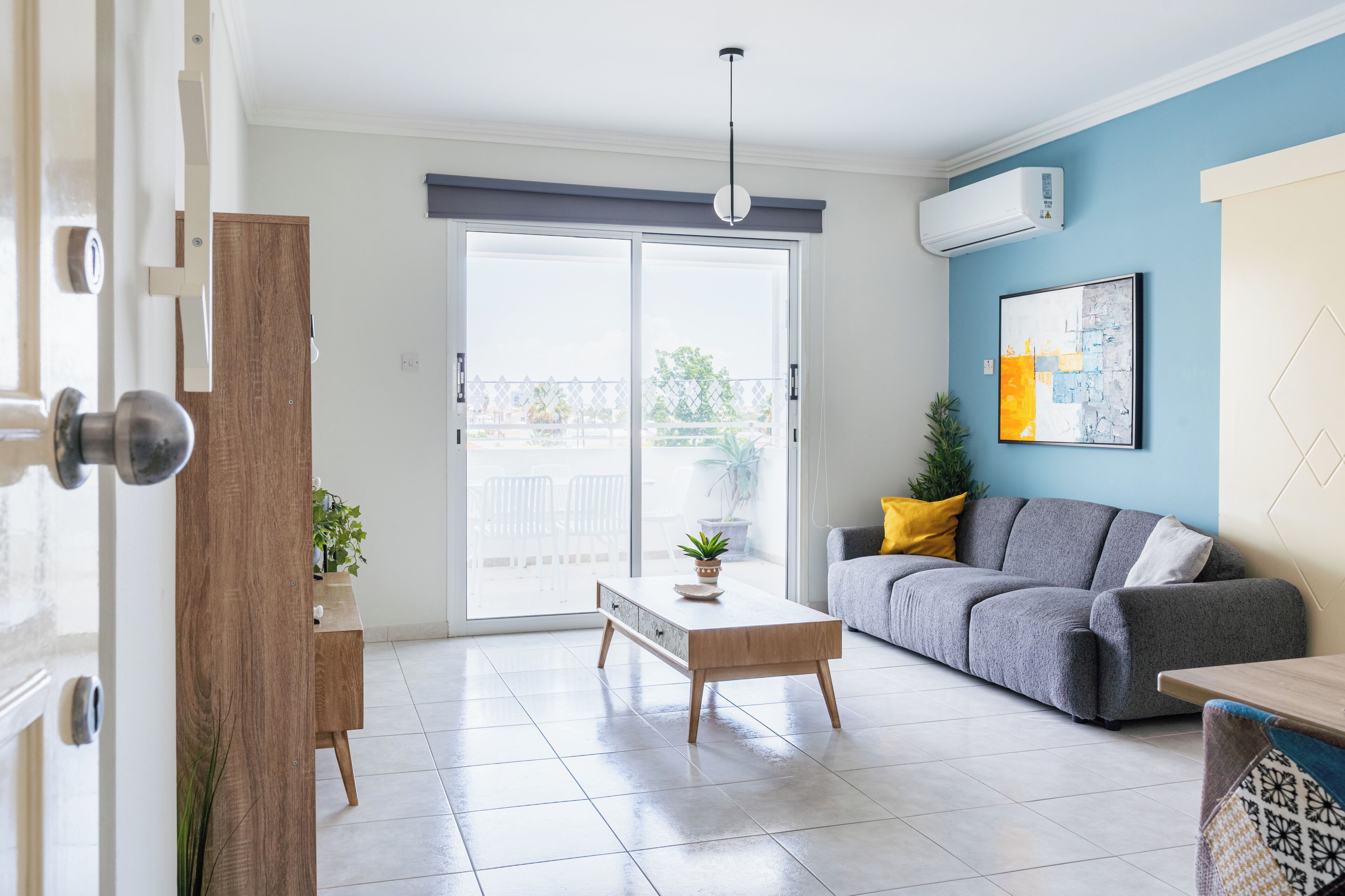 Una sala de estar moderna con una puerta corrediza de vidrio, un sofá gris, una mesa de centro de madera y una pared de acento azul.
