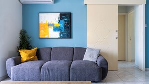 A living room with a grey sofa, a framed abstract painting, and a door with a geometric design. - Sweet Retreat 2-BR Apt. in Mackenzie (Larnaca)