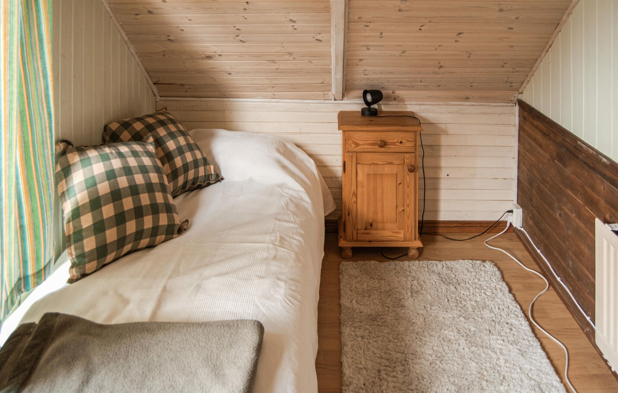 A bedroom with a bed, checkered pillows, a wooden cabinet, and a white rug.