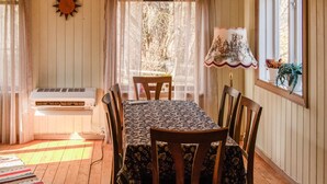 Un comedor con una mesa dispuesta para cuatro personas, una ventana con vistas a árboles, un adorno de sol en la pared y una lámpara con pantalla estampada.