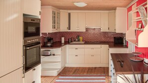 Una cocina con armarios blancos, salpicadero de baldosas rojas, suelo de madera y alfombra a rayas.
