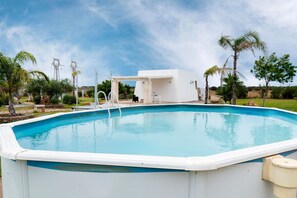 A swimming pool with a white deck, a covered seating area, and palm trees in the background. - La Pennichella Apartments - La Pennichella Apartments - Terra (Nardo)