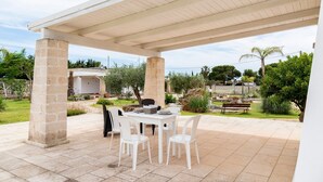 Eine überdachte Terrasse mit Tisch und Stühlen, Steinsäulen und Blick auf den umliegenden Garten.