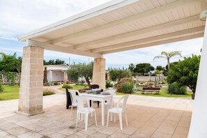 A covered patio with a table and chairs, stone pillars, and a view of the surrounding garden. - La Pennichella Apartments - La Pennichella Apartments - Terra (Nardo)