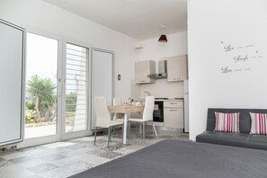 A modern, well-lit room with a dining area, kitchen, and a large sliding glass door leading to a garden. - La Pennichella Apartments - La Pennichella Apartments - Terra (Nardo)
