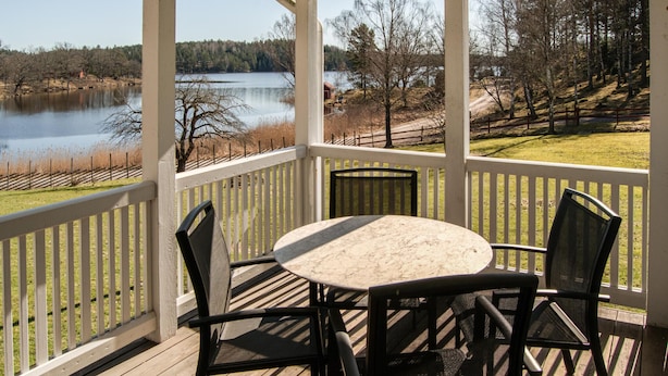 Un espace extérieur abrité, doté d’une table et de chaises, qui offre une vue sur un lac et une zone boisée.