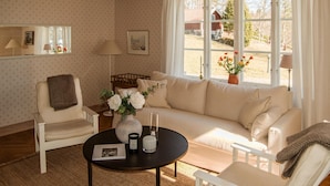 Un salon chaleureux avec un canapé, des fauteuils, une table basse et une vue sur une grange rouge, visible à travers de grandes fenêtres.