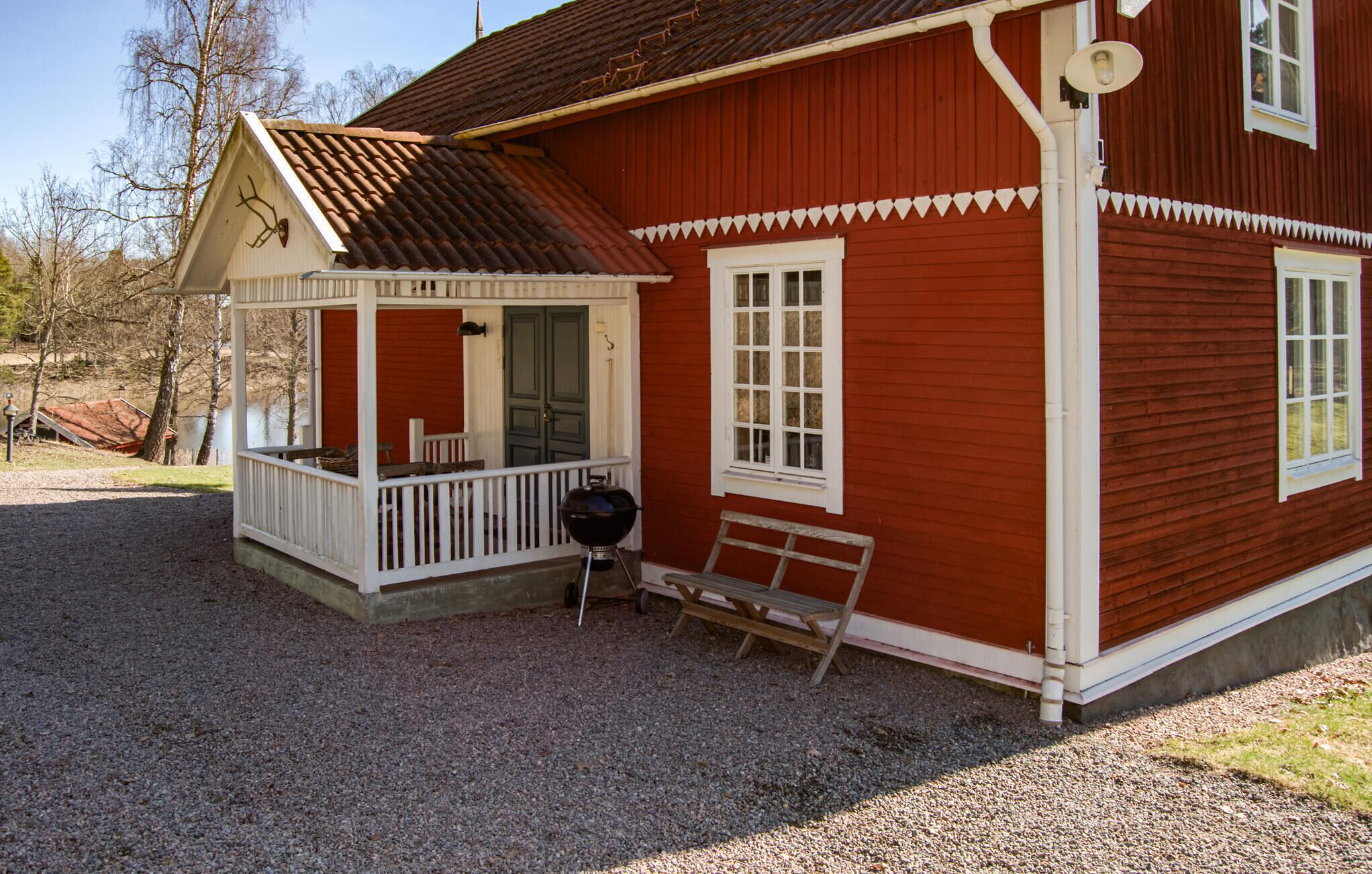 Une maison en bois rouge avec un porche, un banc et un barbecue.