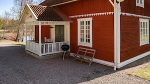 Une maison en bois rouge avec un porche, un banc et un barbecue.