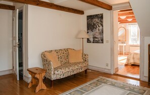 Ein Zimmer mit einem blumigen Sofa, einem Holzschemel, einer Lampe und einem Poster an der Wand.