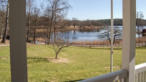 Vue sur un lac depuis une véranda dotée d’une balustrade en bois, avec une zone herbeuse et des arbres sans feuilles.