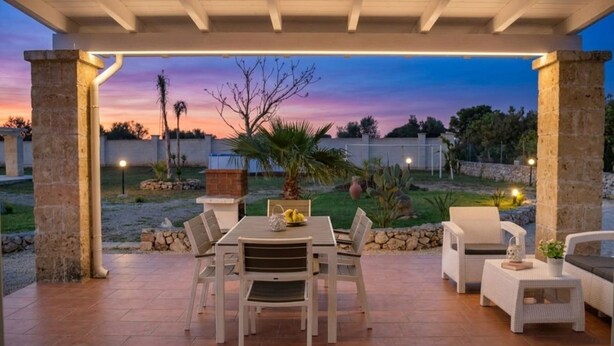 Un patio cubierto con una mesa, sillas, una planta en maceta y vistas del paisaje circundante.