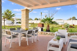 Une terrasse extérieure avec un pilier en pierre, une table avec des chaises et une petite table blanche agrémentée d’une plante.