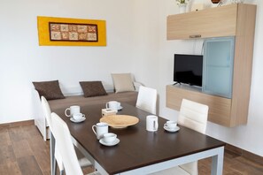 Un coin repas avec une table en bois, des chaises blanches et un téléviseur fixé au mur.
