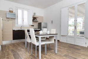 A compact kitchen with a dining area, a refrigerator, and a window. - La Pennichella Apartments - La Pennichella Apartments - Sole (Nardo)