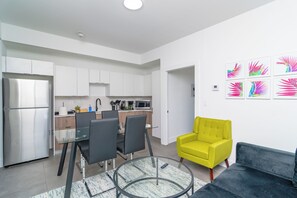 Une cuisine moderne avec des meubles blancs, un réfrigérateur en acier inoxydable et un coin repas comprenant une table et des chaises en verre.