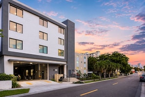 A modern multi-story building with a flat facade, large windows, and a visible entrance with a staircase.