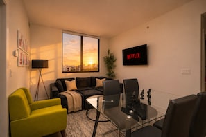 A modern living room with a sofa, chairs, a coffee table, and a large window with a sunset view. - Miami City Escape 2BR Suite Near Brickell & Miami Beach (Miami)