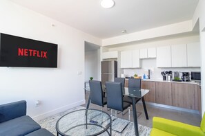A modern apartment with a living area featuring a flat-screen TV, a dining table with chairs, a kitchen with white cabinets, and a small island. - Miami City Escape 2BR Suite Near Brickell & Miami Beach (Miami)