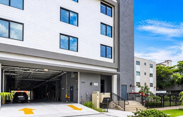 A modern building with a covered parking area, a staircase leading to the entrance, and a clear sky.