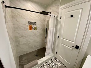 Ein Badezimmer mit Duschbereich, einer Tür und einem gemusterten Boden.