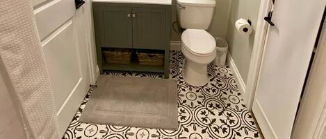 A bathroom with a sink, mirror, toilet, patterned floor, and towel rack.