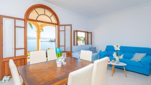 Una habitación con una mesa de comedor de madera, sillas blancas, un sofá azul y vistas al mar.