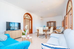 Ein Wohnzimmer mit Fernseher, Sofa, Esstisch und Stühlen.