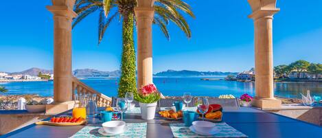 Ein Tisch reichhaltig mit Frühstücksleckereien gedeckt, mit Blick auf das Meer und einer Palme.