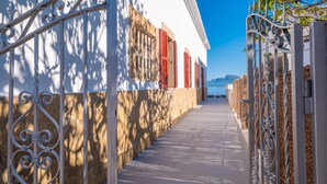 Un estrecho callejón con puertas metálicas ornamentales y un edificio con contraventanas rojas.