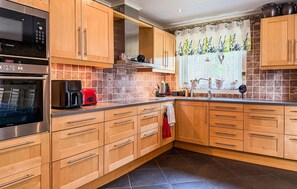 A modern kitchen with wooden cabinets, a stainless steel oven, a coffee maker, and a window with a floral curtain. - 2 bedroom nice home in Bergsäng (Bergsäng)