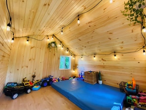 A wooden room with a blue mat, string lights, toys, and a window. - Your Sweet Home in Pitt with King Beds and Free Parking near City (Pittsburgh)