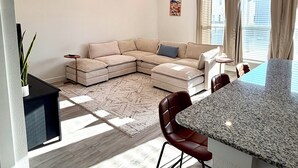 En moderne stue med en modulsofa, et spiseområde med en granitbordplade, og et køkken med indbygget ovn.