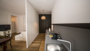 Een moderne keuken met een ingebouwde kookplaat, een eetgedeelte met een houten tafel en stoelen, en een witte bank in een woonruimte.