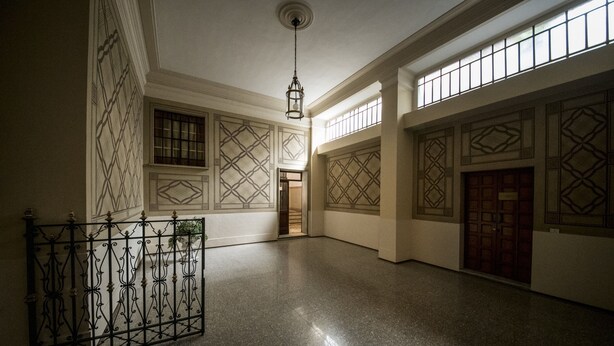 Een interieur met een gepolijste vloer, decoratieve ijzeren balustrades en een behang met patroon.
