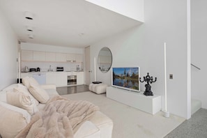 A modern living room with a sofa, a television, and a decorative item on a stand. - Darlinghurst Retreat with Stunning Skyline Views (Darlinghurst)