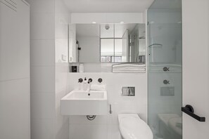 A modern bathroom with a glass shower enclosure, a white sink, and a toilet. - Darlinghurst Retreat with Stunning Skyline Views (Darlinghurst)