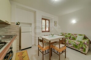 A compact kitchen with a dining table and chairs, a refrigerator, and a sofa with a floral pattern.