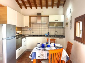 A compact kitchen with a refrigerator, stove, microwave, and a dining table set for four. - Casa degli Ulivi - Lacona (Capoliveri)
