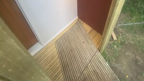 Een kamer met een witte muur, een houten deur, een klein zwart voorwerp aan de muur, en een schuin plafond met een lamp.