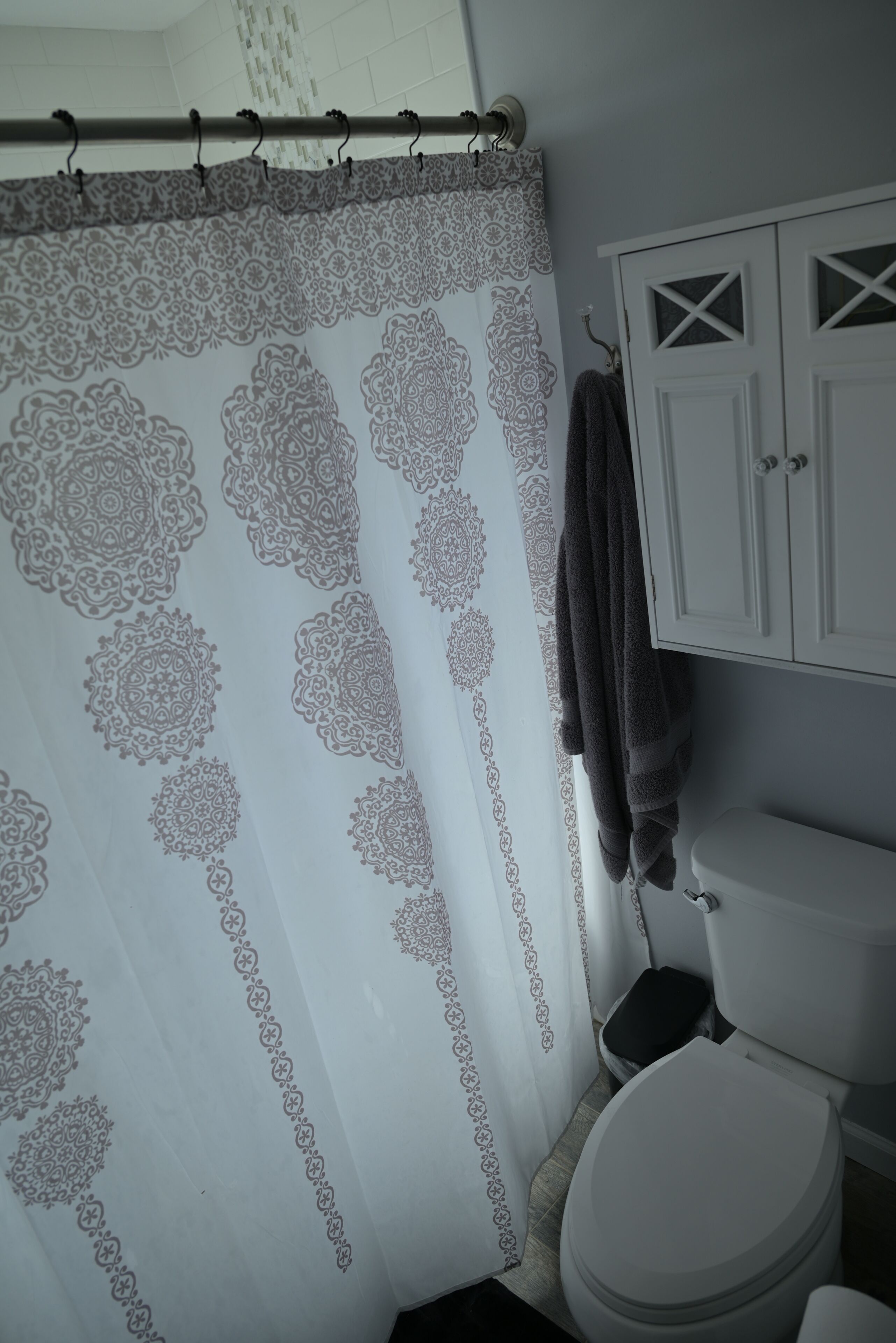 A bathroom with a patterned shower curtain, a white toilet, and a cabinet with a cross design.