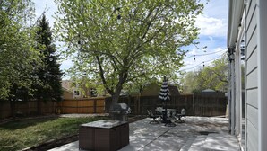 Un patio trasero con una parrilla, muebles de exterior y un árbol.